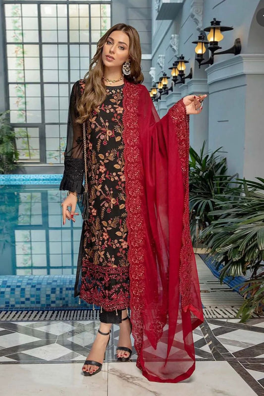 Woman in a black floral dress with a red dupatta standing in an elegant indoor setting.